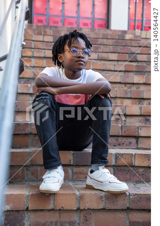 African american teenage boy leaning on rail on brick steps with glasses and white sneakers African american teenage boy leaning on rail on brick steps with glasses and white sneakers 140564427