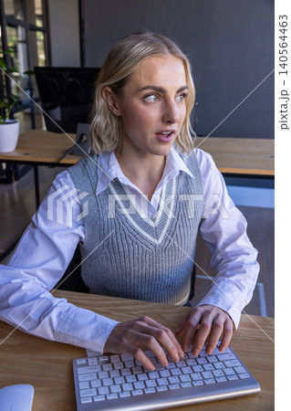 Female office worker typing on wireless keyboard at office desk with mouse and monitors Female office worker typing on wireless keyboard at office desk with mouse and monitors 140564463