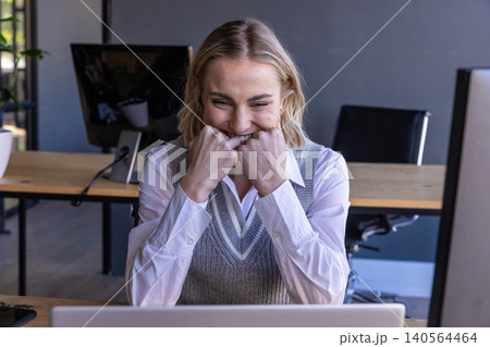 Businesswoman biting fists near mouth in excitement at office desk with laptop monitors 140564464