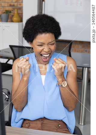 African American woman sitting at office desk using computer monitor and whiteboard African American woman sitting at office desk using computer monitor and whiteboard 140564487