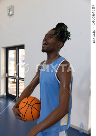 African american male wearing jersey standing on gym court holding ball sweating at exit doors 140564507