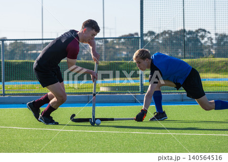 Two male field hockey players vying for ball with sticks on synthetic turf pitch Two male field hockey players vying for ball with sticks on synthetic turf pitch 140564516