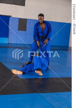 African american male training partners grappling on blue mats at martial gym with gis African american male training partners grappling on blue mats at martial gym with gis 140564521