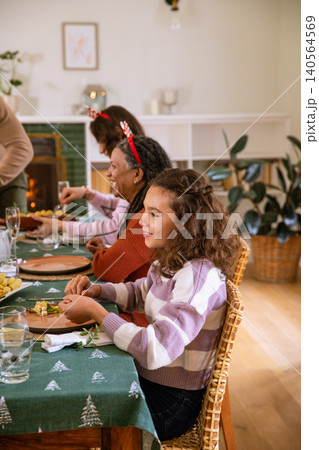Diverse family gathering around table with reindeer headbands, eating by fire, copy space 140564569