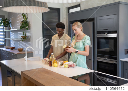 Diverse couple unpacking mesh bags of lemons, cooking oil on kitchen island under pendant lights Diverse couple unpacking mesh bags of lemons, cooking oil on kitchen island under pendant lights 140564652