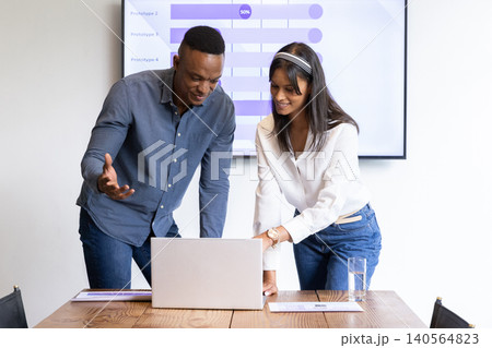 Diverse coworkers leaning over laptop at conference table reviewing bar chart on display Diverse coworkers leaning over laptop at conference table reviewing bar chart on display 140564823
