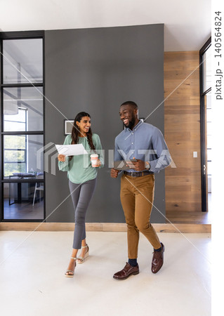 Diverse coworkers walking in business attire in office corridor with coffee, documents, tablet 140564824