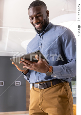 African american man standing in office holding tablet and wearing wristwatch, leather belt 140564825