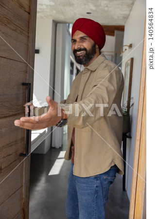 Mid adult indian man opening wooden door with metal handle, extending arm in home entrance Mid adult indian man opening wooden door with metal handle, extending arm in home entrance 140564834