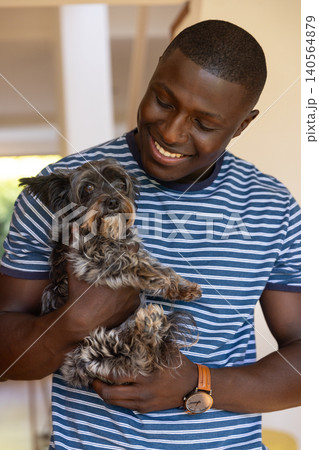 African american man holding small gray and black dog in warmly lit home 140564879