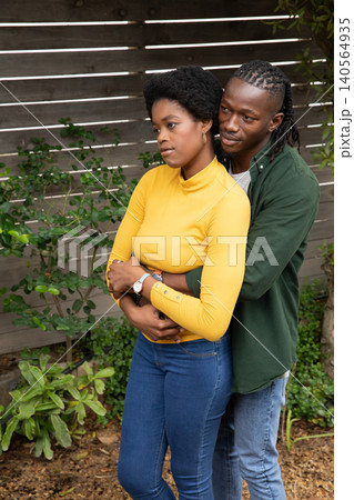 African american couple hugging in garden by wooden fence with woman's wristwatch, green shrubs African american couple hugging in garden by wooden fence with woman's wristwatch, green shrubs 140564935