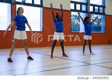 Diverse female students warming up in school gym on wooden court with lines and windows Diverse female students warming up in school gym on wooden court with lines and windows 140565001
