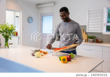 African american man tipping peppers off board into bowl at kitchen island, copy space African american man tipping peppers off board into bowl at kitchen island, copy space 140565018