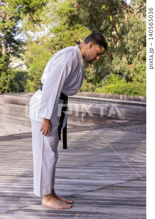 Adult man wearing white martial arts gi and black belt, bowing on deck outdoors Adult man wearing white martial arts gi and black belt, bowing on deck outdoors 140565036