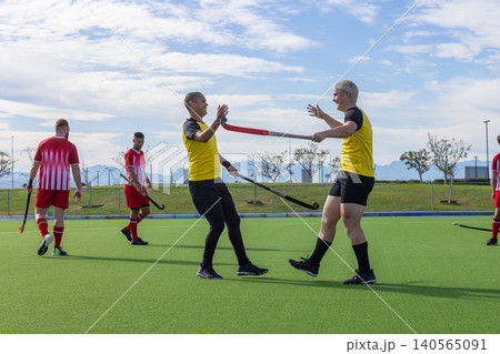 Male players in yellow jerseys celebrating victory on turf field with hockey sticks Male players in yellow jerseys celebrating victory on turf field with hockey sticks 140565091