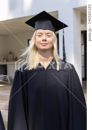 Female graduate standing in front of university porch wearing mortarboard cap, black gown 140565183