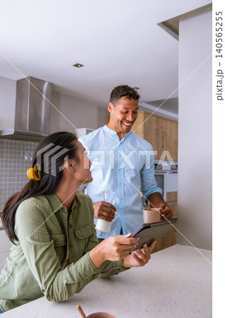 Diverse couple reviewing tablet at kitchen island while holding coffee mug, glass of milk Diverse couple reviewing tablet at kitchen island while holding coffee mug, glass of milk 140565255