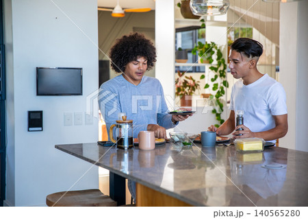 Diverse male friends making breakfast at kitchen island with smartphone and seasoning avocado toast Diverse male friends making breakfast at kitchen island with smartphone and seasoning avocado toast 140565280