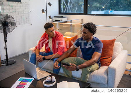 Diverse male colleagues discussing design concepts over laptop and phone mockups in office lounge Diverse male colleagues discussing design concepts over laptop and phone mockups in office lounge 140565295