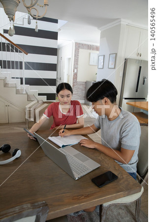 Asian students studying together at open-plan kitchen table using laptop tablet notebook headphones Asian students studying together at open-plan kitchen table using laptop tablet notebook headphones 140565496
