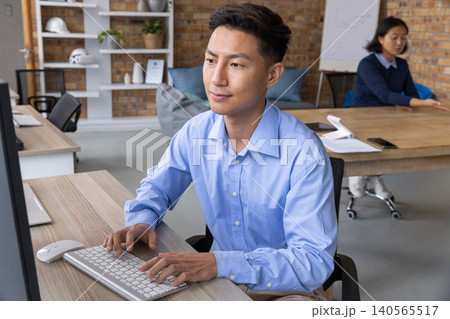 Asian coworkers typing on keyboard at open-plan office desk, light-blue shirt visible Asian coworkers typing on keyboard at open-plan office desk, light-blue shirt visible 140565517
