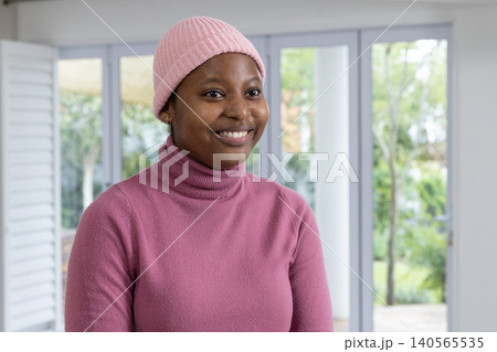 African American woman standing in bright room by glass doors wearing pink beanie and turtleneck African American woman standing in bright room by glass doors wearing pink beanie and turtleneck 140565535