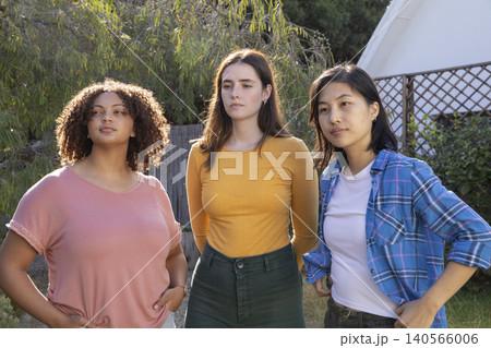 Diverse female friends standing in backyard amid garden shrubs, lattice trellis and wooden fence Diverse female friends standing in backyard amid garden shrubs, lattice trellis and wooden fence 140566006