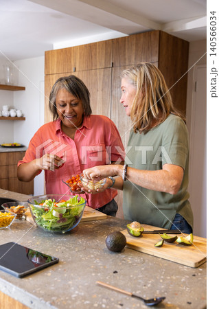 Diverse female friends preparing salad at kitchen island using tablet, cherry tomatoes 140566034