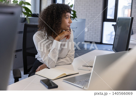 African american woman resting chin on hand and gazing right at white desk in office with notebook African american woman resting chin on hand and gazing right at white desk in office with notebook 140566069