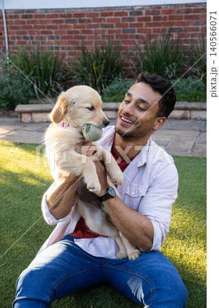 Man cross-legged on backyard lawn with golden retriever puppy with tennis ball 140566071