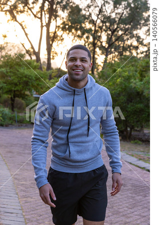African american man walking along paved path in park at dusk wearing hoodie, black shorts 140566079
