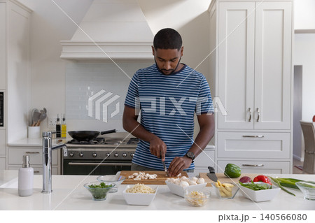 African american man slicing mushrooms in home kitchen at island with chef knife and bowls 140566080