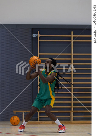 African american man playing basketball in green and yellow uniform on court by wall bars African american man playing basketball in green and yellow uniform on court by wall bars 140566148