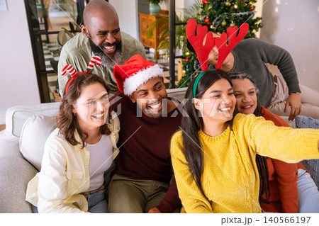 Diverse family taking holiday selfie on couch in living room with smartphone, christmas tree 140566197