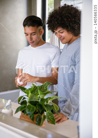Diverse male friends opening grooming jar at bathroom counter next to toothbrush holder and plant Diverse male friends opening grooming jar at bathroom counter next to toothbrush holder and plant 140566335