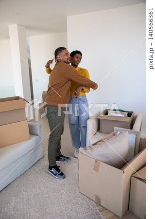 Diverse couple hugging in empty living room surrounded by moving boxes with bubble wrap near sofa Diverse couple hugging in empty living room surrounded by moving boxes with bubble wrap near sofa 140566361