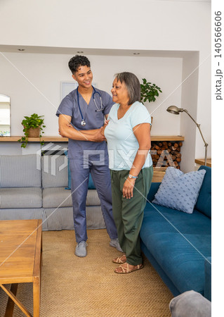 Asian male caregiver supporting senior woman standing by sofa in living room with stethoscop Asian male caregiver supporting senior woman standing by sofa in living room with stethoscop 140566606