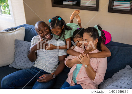 Diverse family laughing and playing on sofa in living room with pillows and books 140566625