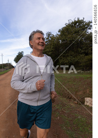Man jogging on dirt road wearing hoodie, crewneck shirt, athletic shorts and running shoes 140566816