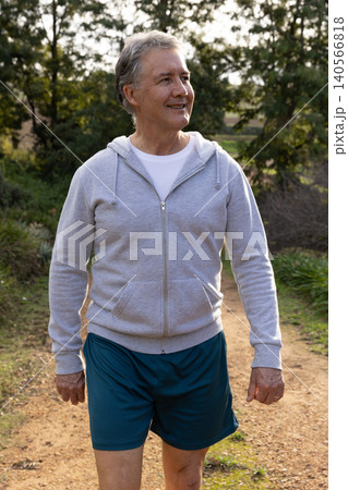 Senior man walking along dirt trail in park wearing gray hoodie, teal shorts, copy space Senior man walking along dirt trail in park wearing gray hoodie, teal shorts, copy space 140566818