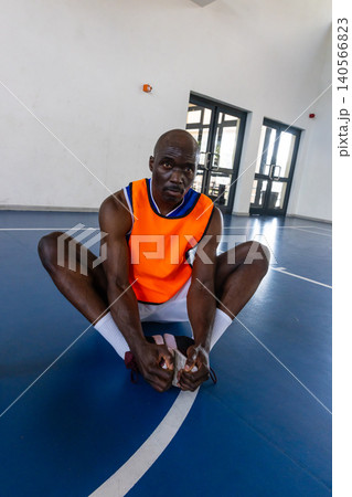 African american male athlete stretching legs on court wearing orange bib and pink sneakers African american male athlete stretching legs on court wearing orange bib and pink sneakers 140566823