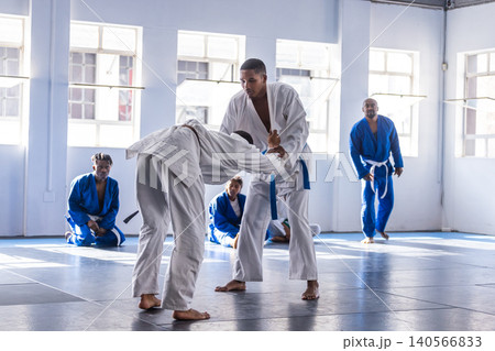 Male martial arts students grappling in bright dojo on padded mats with gis and belts Male martial arts students grappling in bright dojo on padded mats with gis and belts 140566833