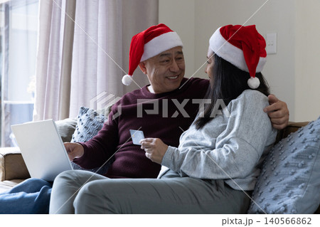 Asian couple in santa hats sitting on sofa in living room using laptop, credit card Asian couple in santa hats sitting on sofa in living room using laptop, credit card 140566862