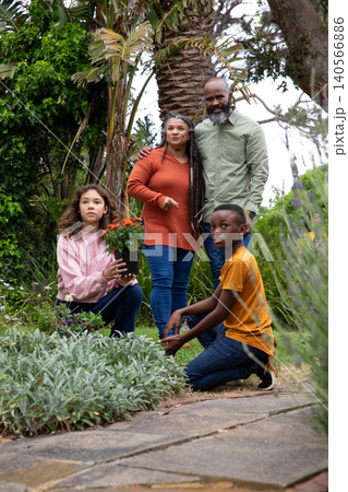 African american senior couple gardening with diverse kids tending pot of blooms on walkway 140566886