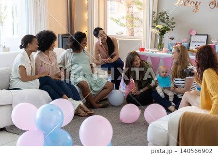 Diverse female friends celebrating baby shower in living room with balloons, baby, camera 140566902