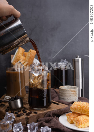 Pour milk make latte coffee, Asian iced coffee in transparent glass and roasted coffee beans and Crispy Pie on wood. black background studio photo, Copy space for your text Pour milk make latte coffee, Asian iced coffee in transparent glass and roasted coffee beans and Crispy Pie on wood. black background studio photo, Copy space for your text 140567208