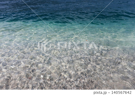 A refreshing view of shallow, pristine water with rippling waves and a clear view of the stony substrate beneath the surface. 140567642