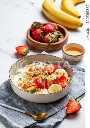 Natural Greek yogurt with granola, banana and strawberries in a bowl on a marble background Natural Greek yogurt with granola, banana and strawberries in a bowl on a marble background 140569337