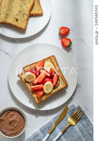 Toasted bread with chocolate cream, strawberries, and banana on a plate on a marble background Toasted bread with chocolate cream, strawberries, and banana on a plate on a marble background 140569345