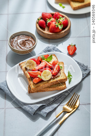 Toasted bread with chocolate cream, strawberries, and banana on a plate on a tile background Toasted bread with chocolate cream, strawberries, and banana on a plate on a tile background 140569346
